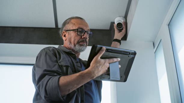 istock Male mature installer sets up CCTV camera in office room using tablet computer 2166740795