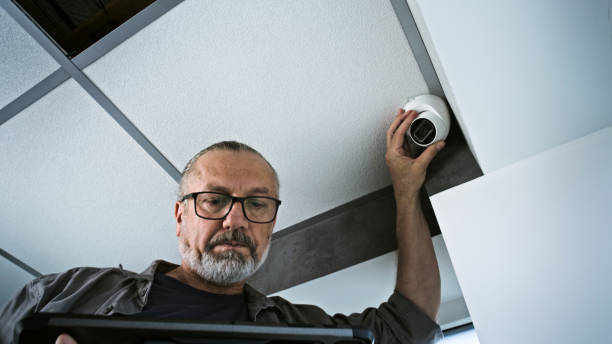 istock Male installer adjusts the angle of CCTV camera in office, uses tablet computer 2166743684