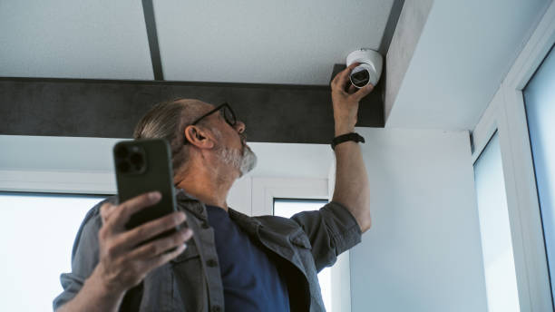 istock Male mature technician sets up CCTV camera in office building using mobile phone 2166744071