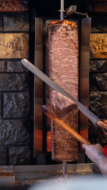 istock Chef slicing meat for shawarma on a vertical rotisserie. Juicy cuts ready 2166744157