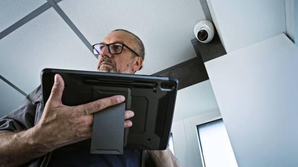 istock Male installer adjusts the angle of CCTV camera in office, uses tablet computer 2166744196