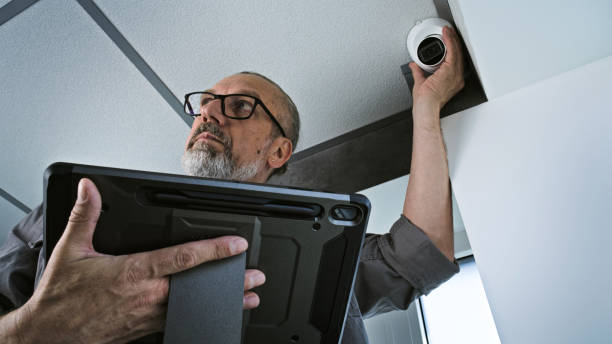 istock Male installer adjusts the angle of CCTV camera in office, uses tablet computer 2166744334