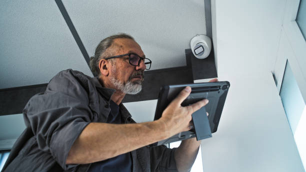 istock Male mature installer sets up CCTV camera in office room using tablet computer 2166746379