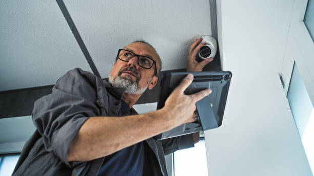 istock Male mature installer sets up CCTV camera in office room using tablet computer 2166746474
