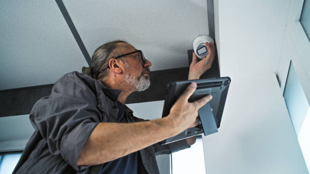 istock Male mature installer sets up CCTV camera in office room using tablet computer 2166746519