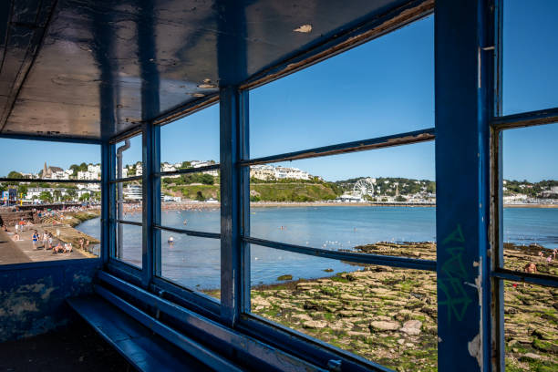 Torquay, UK. 12 August 2024. View of Torquay through a bus shelter with people on the beach.