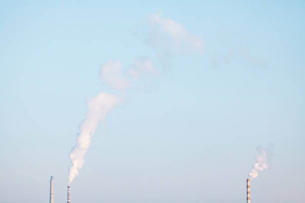 Smokestacks spewing smoke into the sky. Smoke stacks rise against a clear blue sky, showcasing industrial activity and environmental impact