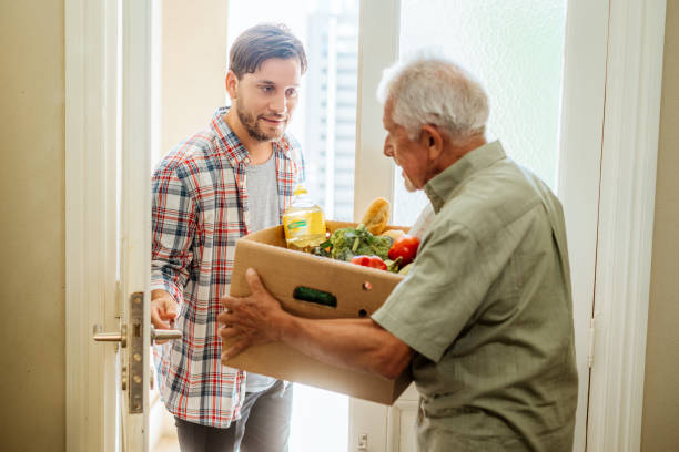 istock Elderly Man Delivering Grocery Box to Young Man's Doorstep 2166771891