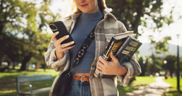 Student, hands and books in park with phone on walk with education, learning or thinking for development at campus. Person, smile and app on path, social media and scholarship at college