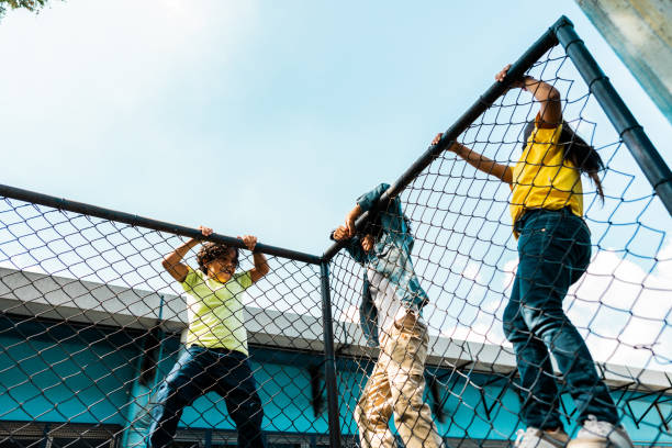 istock Student friends climbing chainlink fence on schoolyard 2166780913