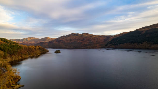 istock Serene lake with a small island, surrounded by autumn-colored hills under a clear sky. 2166780930