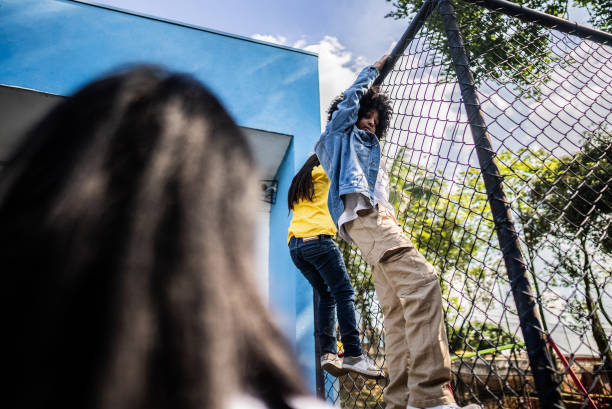istock Student friends climbing chainlink fence on schoolyard 2166781305