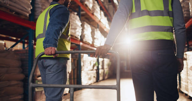 istock Trolley, hands and delivery for logistics in warehouse, back view and teamwork for moving of goods or shipping. Distribution, cargo and people in factory for supply chain, walking and storage 2166784811