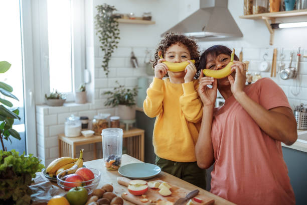 Mother and son posing for a shot while having fun with bananas in a domestic kitchen