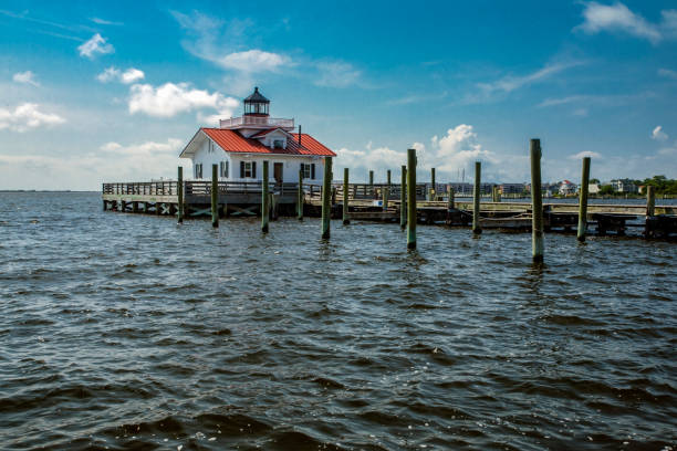 A long exposure photo of the Roanoke Marshes Lighthouse at sunset, giving the water a soft, smooth appearance