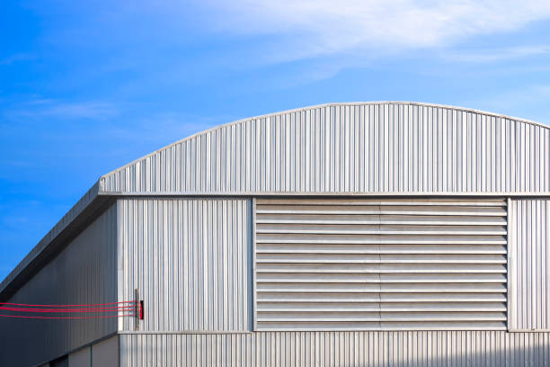 istock Large industrial warehouse with louver ventilation on aluminum corrugated wall with red cable lines wiring into building against blue sky 2166790906