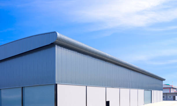 istock Large industrial warehouse building with roller shutter doors on concrete and corrugated aluminum wall in factory area against blue sky background 2166790937