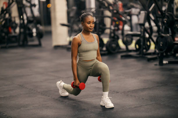 istock A fit active black sportswoman doing lunges with dumbbells at gym. 2166794412