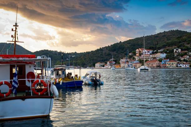 A picturesque view of Vathi, a charming village on the island of Ithaca, Greece, with traditional houses scattered along the lush hillside. The vibrant red-tiled roofs and pastel-coloured buildings contrast beautifully against the green vegetation and the deep blue waters of the Ionian Sea. The peaceful ambience of the village and its surrounding natural landscape create a serene and idyllic coastal scene.