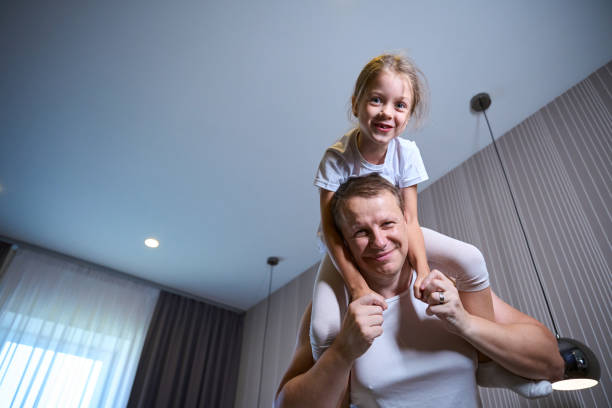 Girl and her dad are having a fun morning get up, the daughter is sitting on her dads shoulders