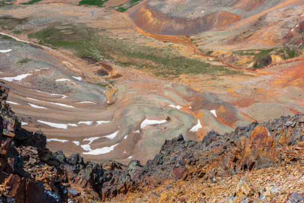 istock Scenic dizzy top-down view from precipice edge with sharp rocks to unusual multicolor stony valley with iron river in sunlight. Colorful awesome alpine scenery with snow in multi-color hilly valley. 2166810354