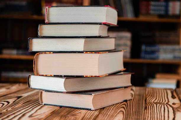 A woman teacher, surrounded by bookshelves in the library, educates university students on literature, utilizing textbooks and information to enhance their studying experience.