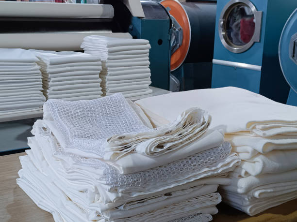 istock Folded white clothes, sheets, tablecloths, in an industrial laundry with machinery behind. 2166814023