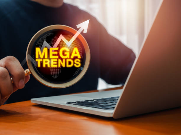 Mega trends, business, technology and marketing trend concept. Text MEGATRENDS with growth graph arrow rise on large magnifying glass in businessman's hand who working with laptop computer on table. mega tendencias, negocios, tecnología y concepto de tendencia de marketing. texto megatrends con la flecha del gráfico de crecimiento en la lupa grande en la mano del hombre de negocios que trabaja con la computadora portátil en la mesa.