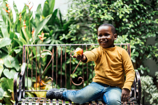 Cheerful black boy eating red apple at home