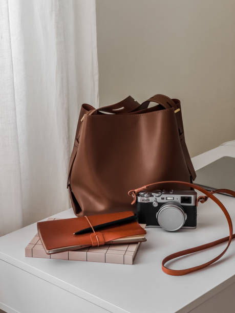 Stylish women's accessories - leather tote bag, notebooks, camera on a white table