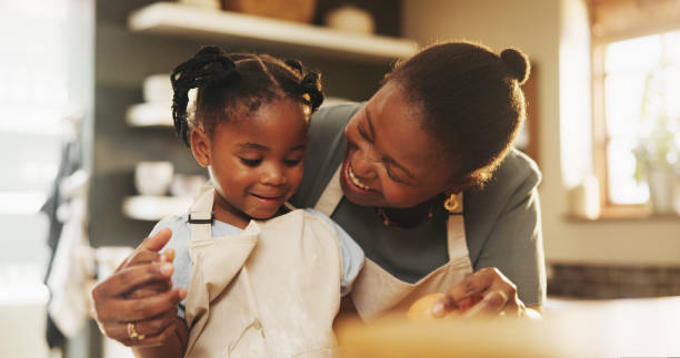 istock Support, child and black mother in kitchen for baking, recipe process and pride at home. Young girl, development and mom at counter for trust, growth and encouragement for making cookies or cake 2166830110