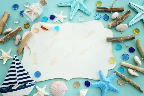 Top view image of boat, starfish, sea glass and empty white board over blue background