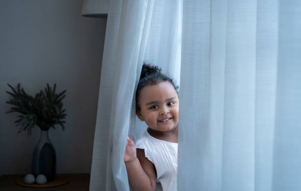 istock A tiny girl plays hide-and-seek with drapes in her bedroom 2166831381