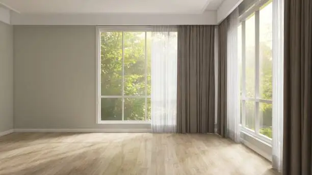 Empty room with gray wall, brown blackout and white sheer curtain in sunlight from backyard with trees on laminated parquet floor