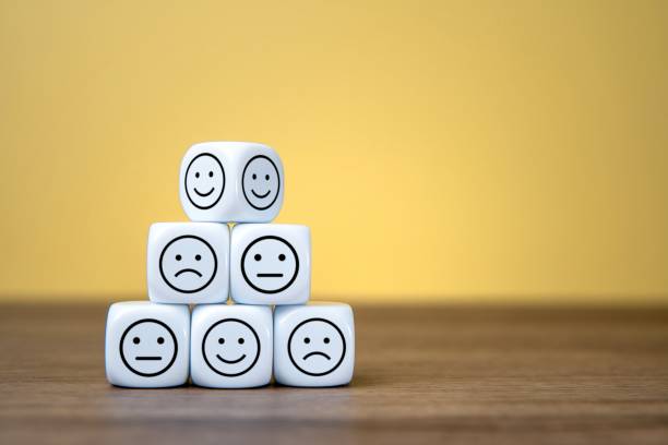White dice with happy, neutral and sad face are stacked on a wooden surface. Copy space for text. Emotion, mood and customer satisfaction concept.