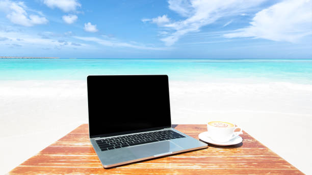 istock Laptop computer and cup of coffee on the table at tropical paradise beach 2166843284