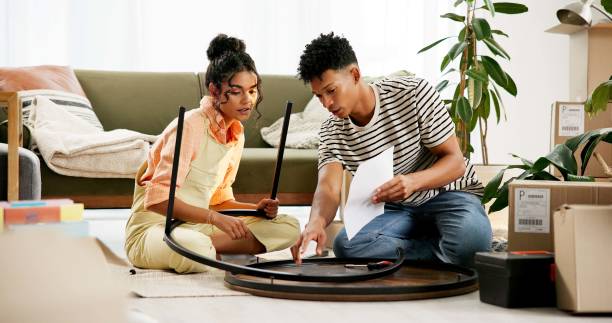 istock Couple, people and assemble table with document for instructions and tips in new home. House, relationship and boxes for moving in with diy, furniture and ownership in living room for renovations 2166844819