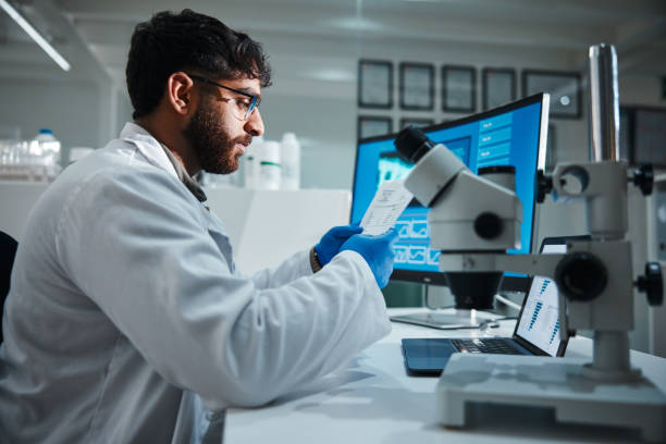istock Computer screen, paper and science with man in laboratory for development, innovation or research. Microscope, results and study with scientist reading at work on medical breakthrough or discovery 2166845349