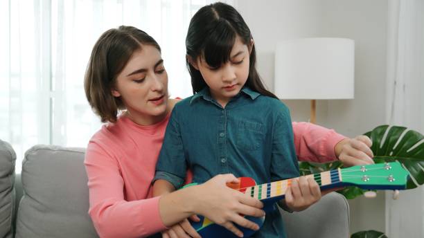 istock Happy girl playing ukulele while caucasian mom teaching and explain. Pedagogy. 2166854929