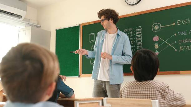 istock Mentor looking around classroom while standing in front of blackboard. Pedagogy. 2166869134