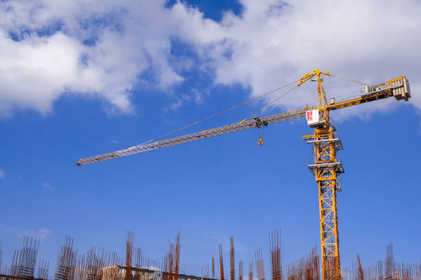 istock yellow tower crane on a background of blue sky with white clouds. Below is a grey concrete building under construction. 2166874027