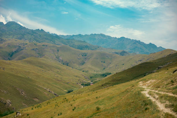 A mountain range with a clear blue sky and a few clouds. The mountains are covered in grass and there is a small village in the valley