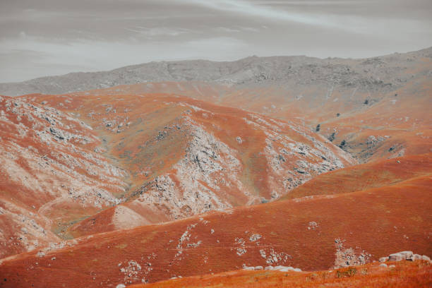 The mountains are covered in orange and brown rocks. The sky is cloudy and the sun is not visible