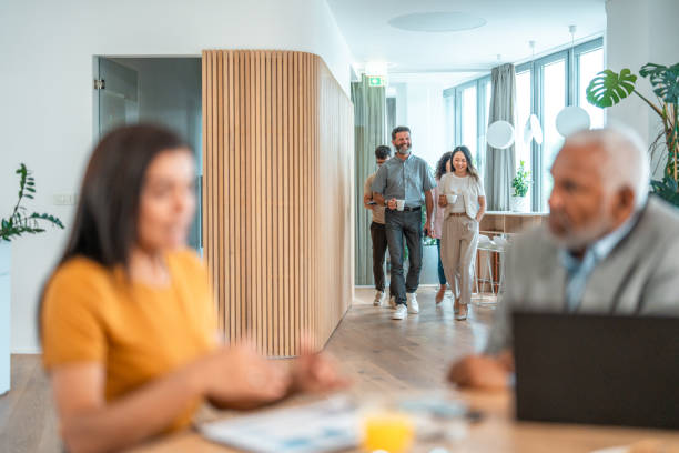 Individuals in a bustling modern office setting, actively working and interacting with laptops and documents. Large windows let in abundant natural light, creating a bright and energetic atmosphere, while some professionals move dynamically through the space, contributing to a vibrant work environment.