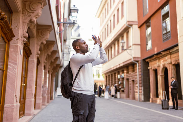 A man takes a photo in a charming European city street during the morning.