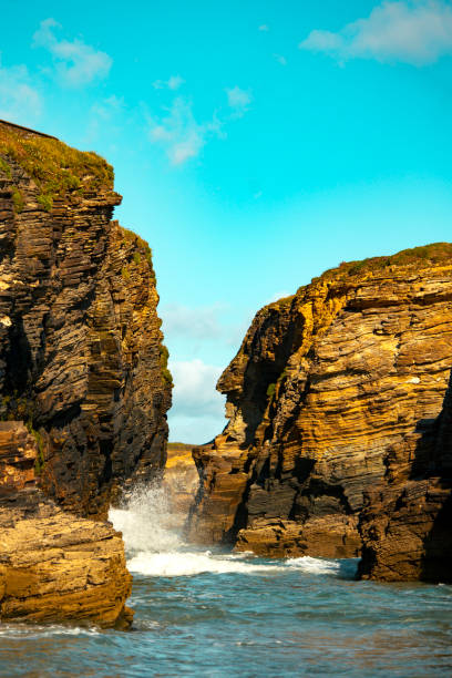 Waves crashing between rugged coastal cliffs with a clear blue sky above .