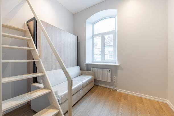 istock Tiny Modern Open Bright Minimalism Home Interior. Couch, Sofa Wardrobe Closet in Background. Dark Brown Flooring. White Cabinets. Stairs to Bedroom. Loft 2166889759