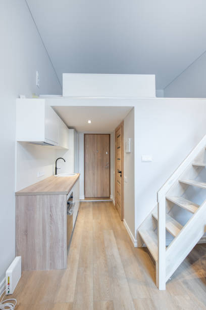 istock Scandinavian Style Tiny Modern Open Bright Minimalism Kitchen Home Interior. Oven, Faucet, and Furniture in Background. Dark Brown Flooring. Flower. White Cabinets. Stairs to Bedroom. Loft 2166889835