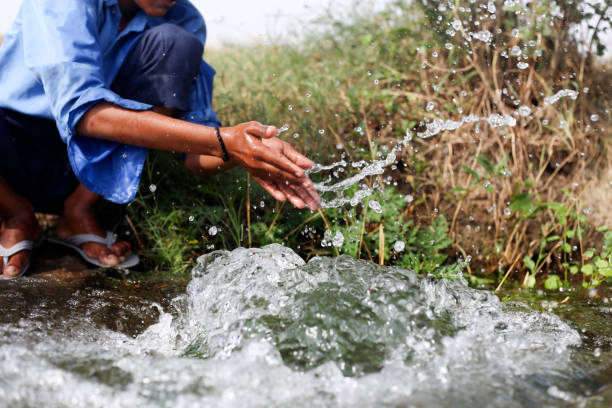 Elementary age school boy washing Hand & feet in flowing water in canal during summer season