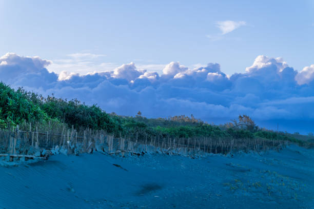 Barbed wire fence ascending a sandy dune with footprints, leading towards a tranquil sea view under a cloudy sky